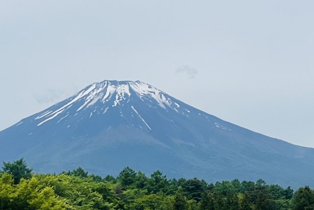 Snow-dusted mountain peak towering over a green forest and a crowded parking lot at the base.