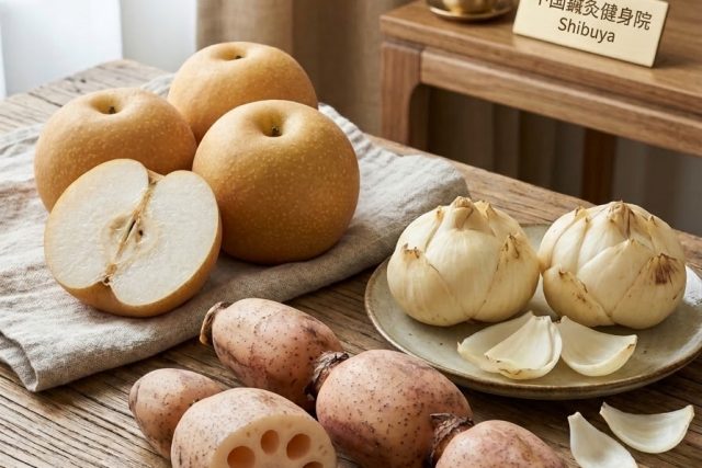 Wooden table with pears, lotus bulbs on a plate, and garlic cloves; a Shibuya sign sits on a wooden desk in the background.